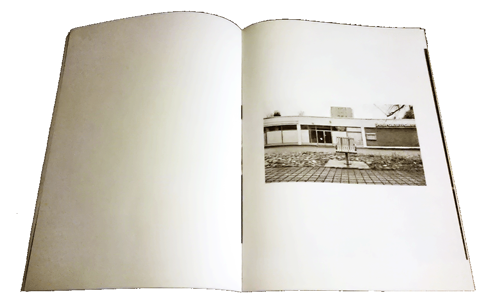 Open zine, one black&white photo of
urban area with empty chair for one person, otherwise the spread is empty.