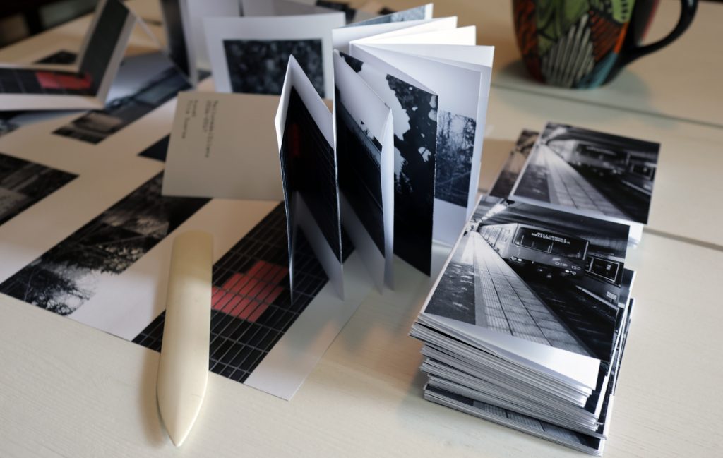 Folded and unfolded zines on table with a bone folder.